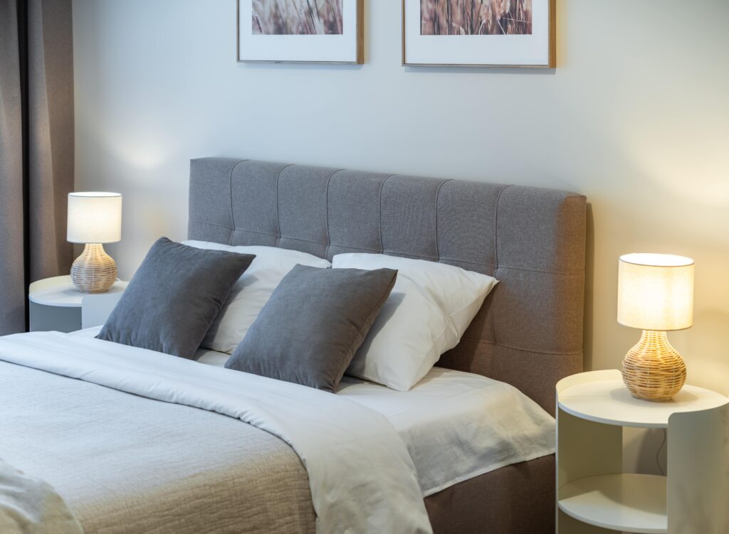 Monteurzimmer mit einem komfortablen Doppelbett, das durch ein graues Polster-Kopfteil und warme Nachttischlampen eine gemütliche Atmosphäre für den Feierabend bietet. Die helle Einrichtung und die modernen Beistelltische unterstreichen den gepflegten Standard der Unterkunft.