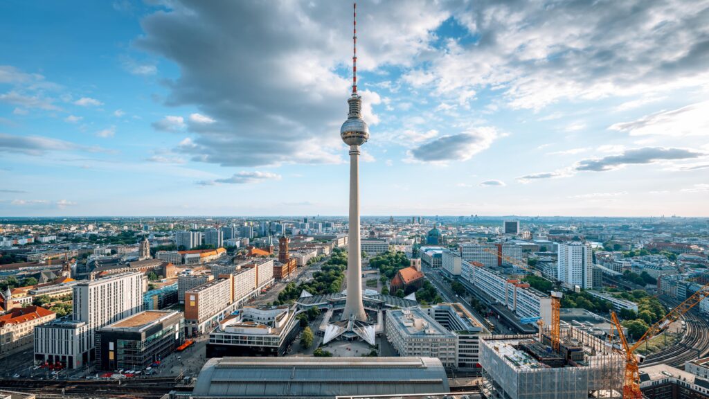 Monteurunterkünfte in Deutschland mieten: Eine beeindruckende Luftaufnahme der Berliner Innenstadt mit dem Fernsehturm als zentralem Orientierungspunkt unter einem weitläufigen Wolkenhimmel.